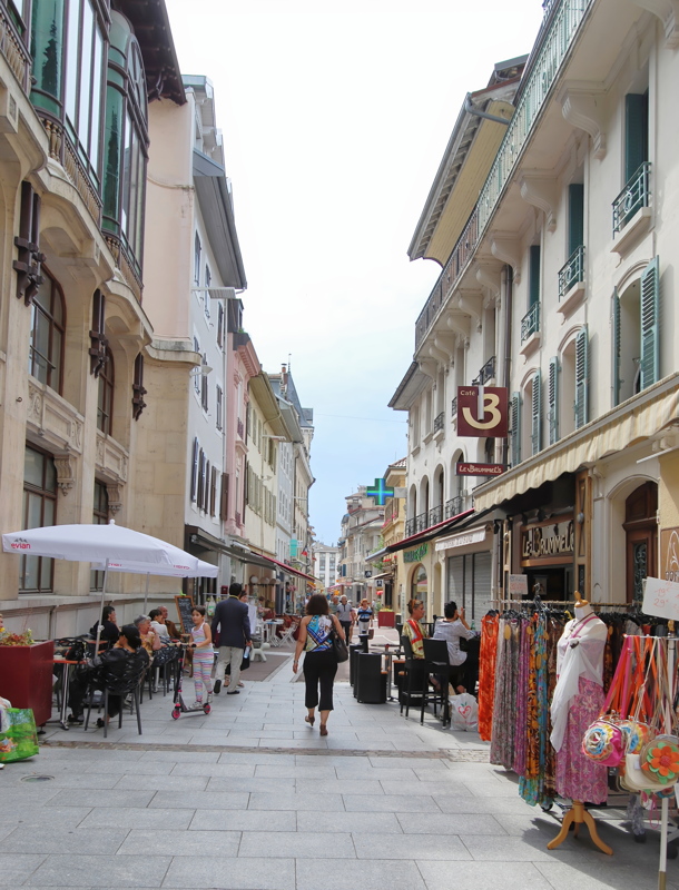 A pedestrian shopping street lined with historic buildings, outdoor cafe seating, and clothing racks, which appears to be Rue Nationale in Évian